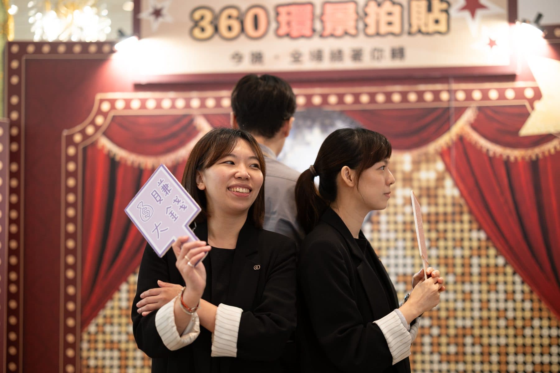 兩位賓客在「360 環景拍貼」復古戲院風格背板前手持道具背對背合影