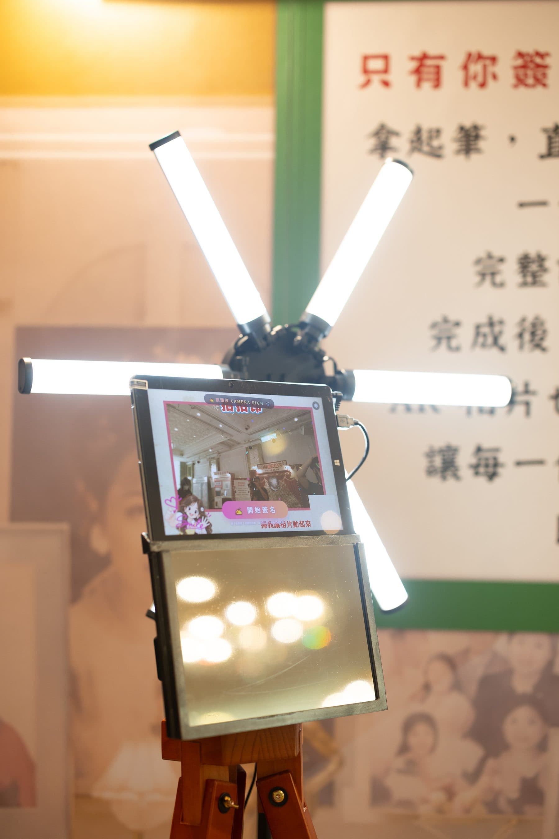 鏡頭簽名機的直式全景,機台架在木質三腳架上,後方為體驗區背板
