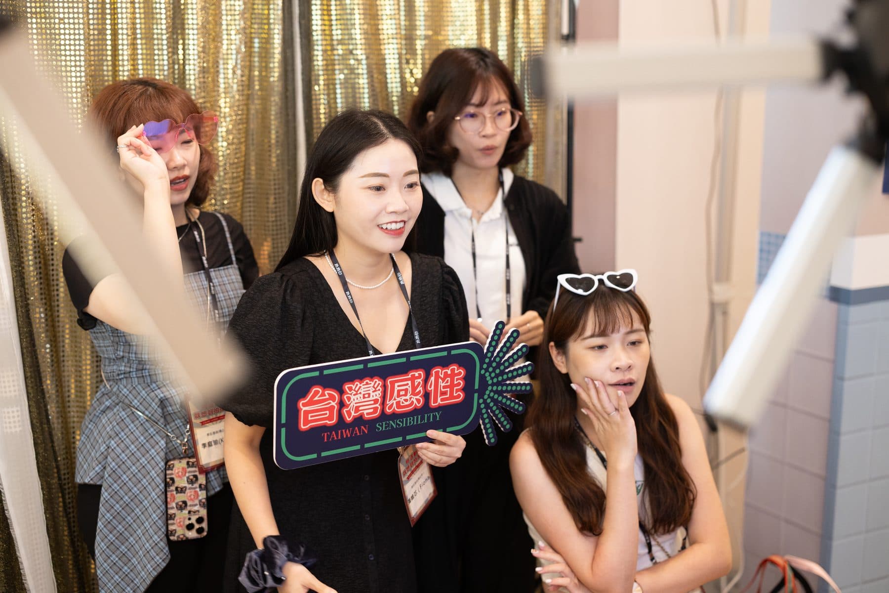 四位賓客在金色亮片背景前手持「台灣感性」霓虹造型手牌與心形眼鏡等道具合影