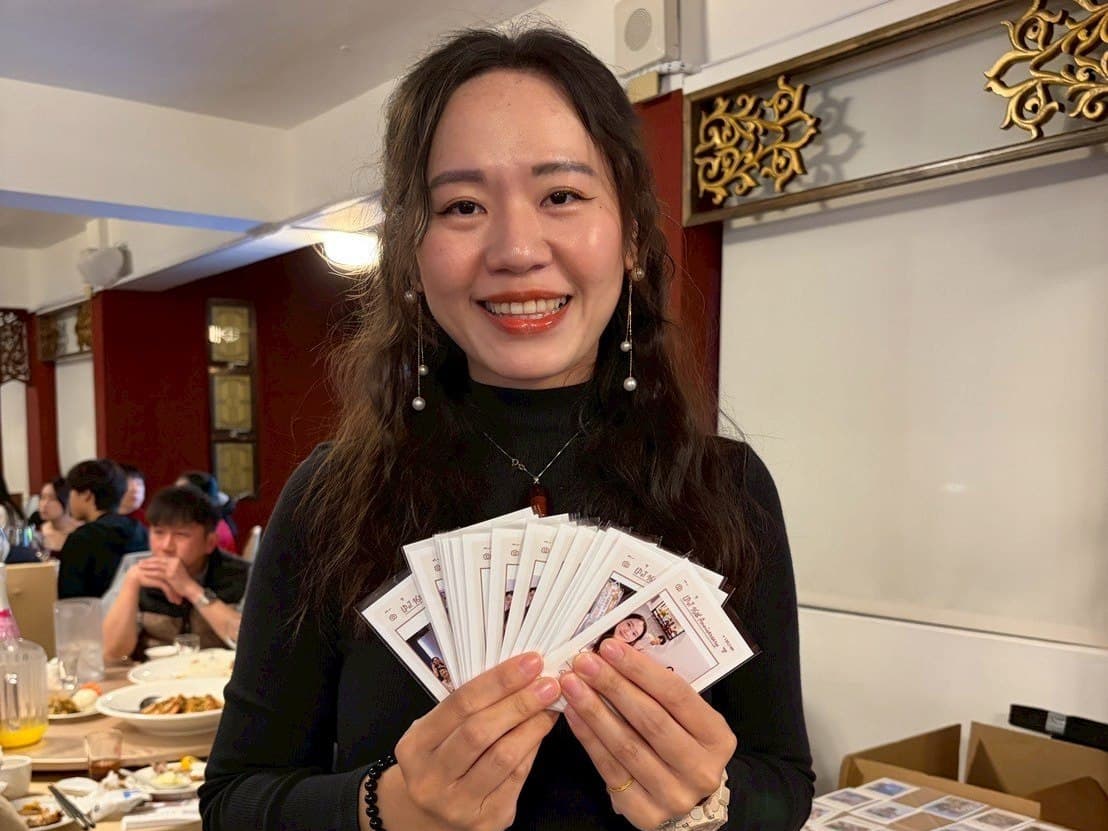 一位賓客在宴會廳中,雙手展開一整疊剛印好的拍貼照片